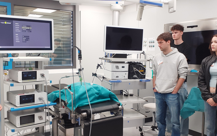 Vier startING Studierende stehen rechts im Bild in einem Operationsraum und schauen auf die Geräte und Displays. Ein Mitarbeiter steht links bei einem Monitor.